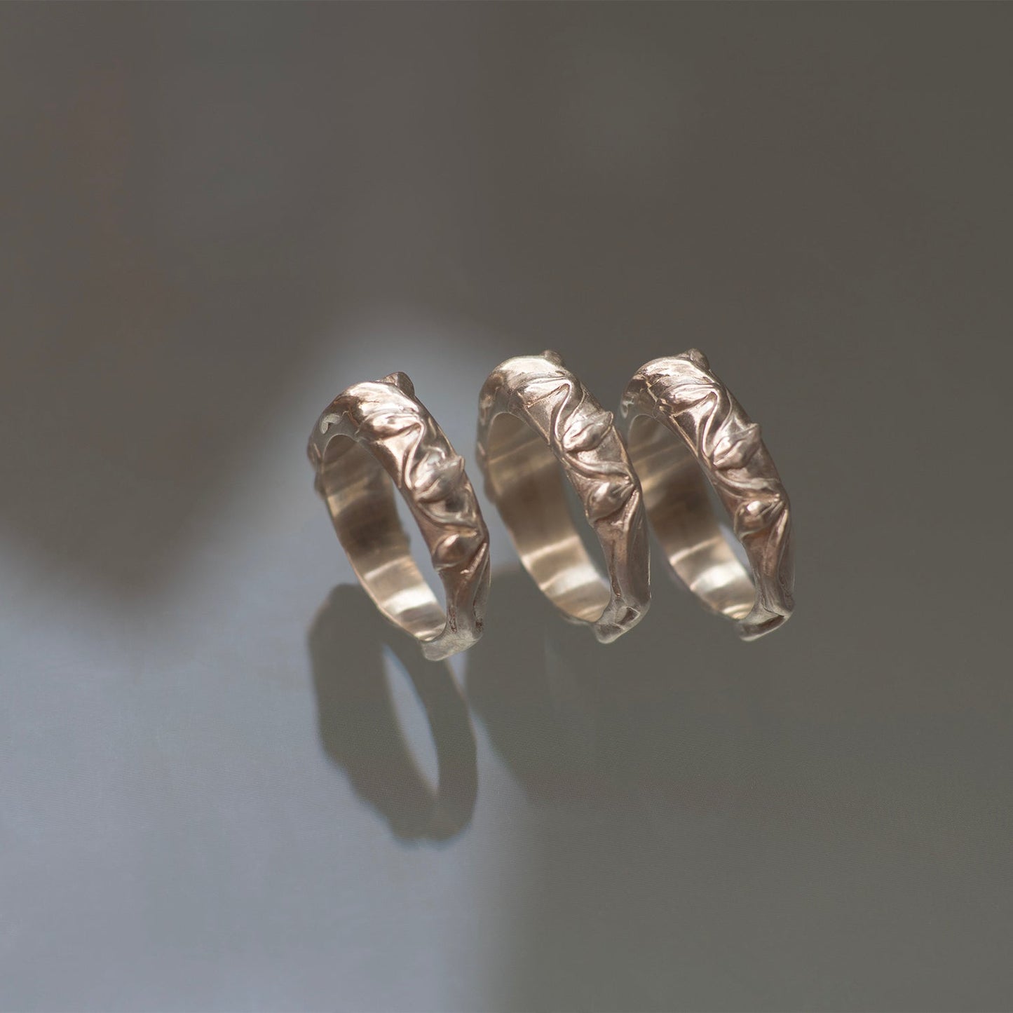 Three silver rings with textured vine leaf surfaces on a gray background