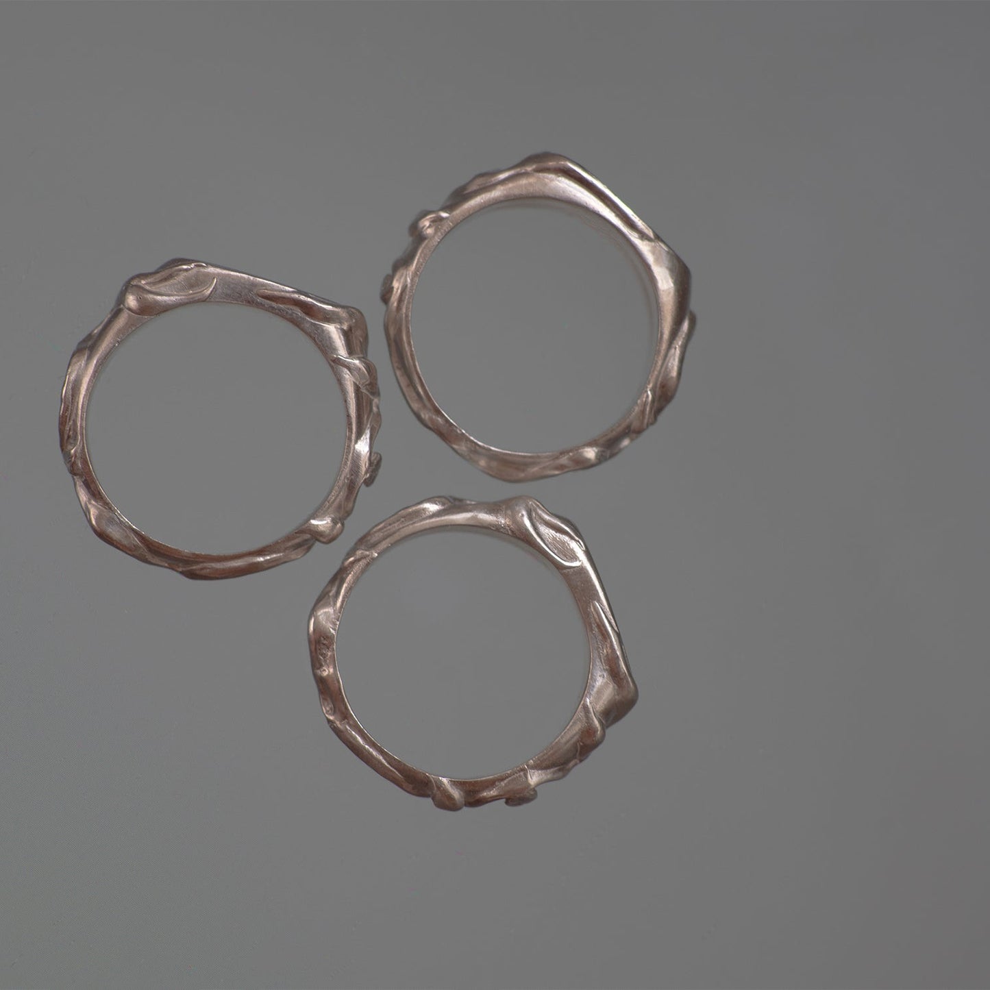 Three silver rings with textured vine leaf surfaces on a gray background