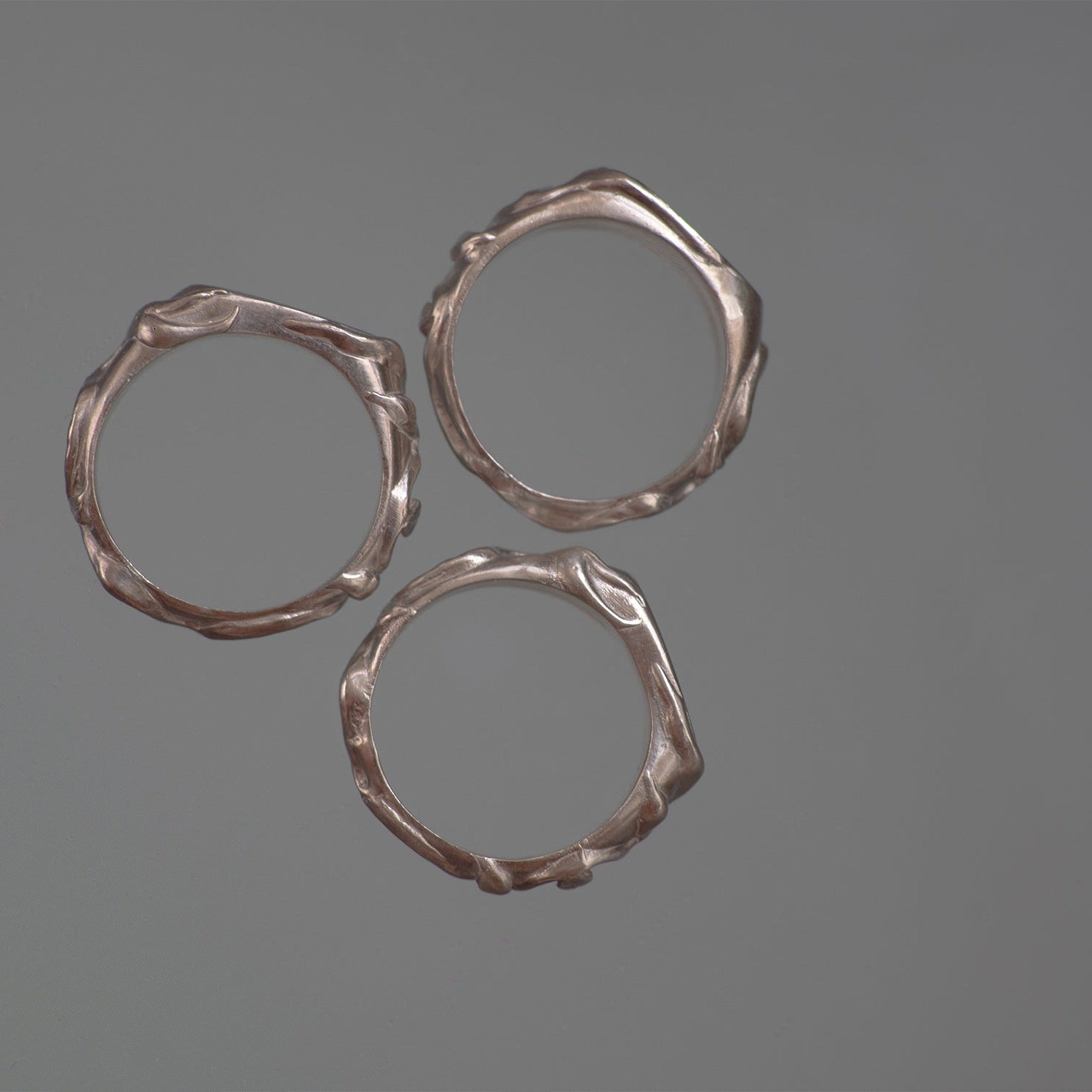 Three silver rings with textured vine leaf surfaces on a gray background