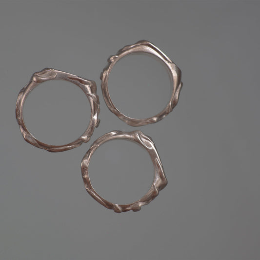 Three silver rings with textured vine leaf surfaces on a gray background